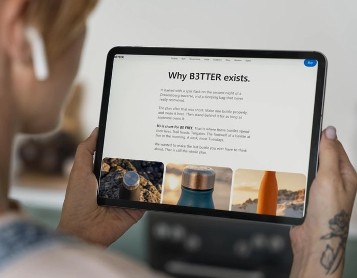 Hands holding an insulated bottle next to a laptop showing the B3TTER site
